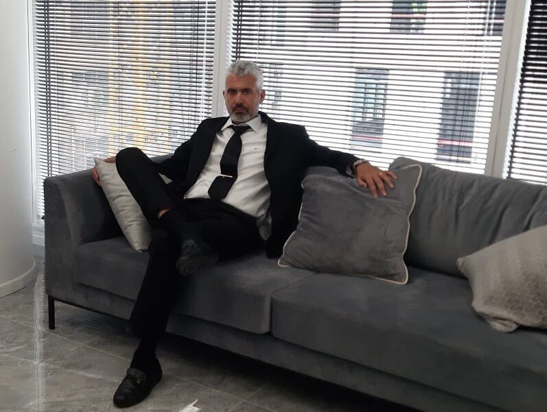 Adv. Shay Zohar sitting in a dark suit on a gray sofa